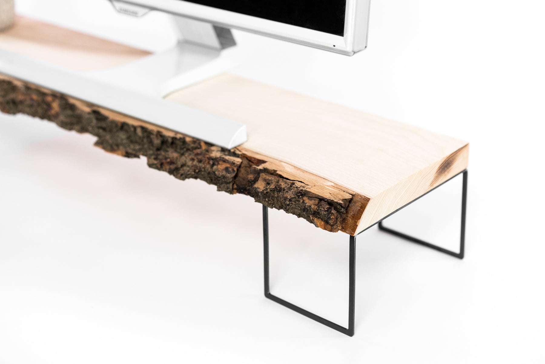 Computer monitor on a live-edge wood stand with an organic bark finish, supported by sleek black metal frame legs.