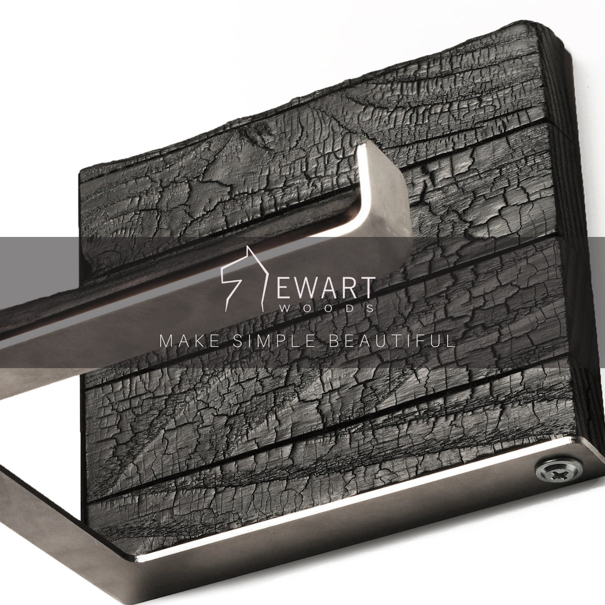 Close-up of a burned ash wood and stainless steel toilet paper holder with the EWART WOODS logo and the slogan MAKE SIMPLE BEAUTIFUL overlaid. The sleek metal bar and textured wood combine for a stylish, functional design.