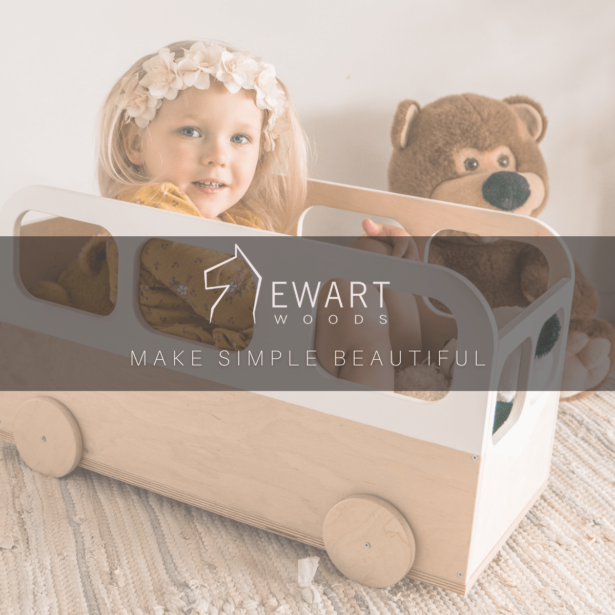 Child playing inside a minimalist wooden bus-shaped storage box, designed with natural wood and white accents. Ewart Woods branding is visible with the slogan &