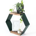 Hexagonal shelf with dark green metal sides and wooden surfaces, featuring a potted plant on the top shelf and a framed minimalist line drawing alongside a reed diffuser on the bottom shelf.