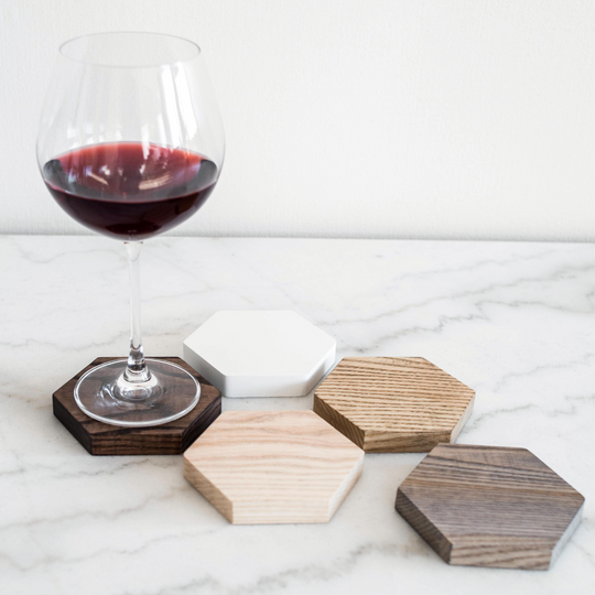 A glass of red wine placed on a hexagonal wooden coaster, surrounded by different-colored wooden coasters, displayed on a marble surface.