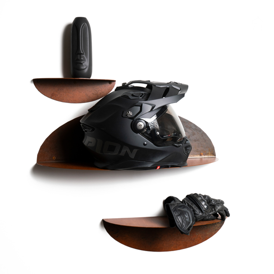 Three curved metal shelves displaying a black motorcycle helmet, gloves, and a decorative moai statue, with a rustic, oxidized finish.