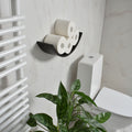 Space-saving dark brown toilet roll holder with a hidden mounting system on a bathroom wall near the toilet, with greenery on the side.