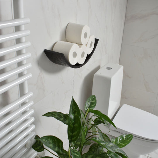 Space-saving dark brown toilet roll holder with a hidden mounting system on a bathroom wall near the toilet, with greenery on the side.
