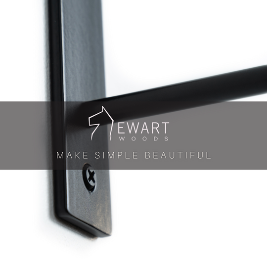 Close-up of a black metal towel rack with a screw and Ewart Woods logo overlay with the slogan &