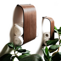 Wall-mounted wooden towel and toilet paper holders with a sleek curved design, elegantly storing rolled towels and paper rolls. Surrounded by greenery.