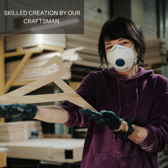 Craftsman holding a wooden hanger with a geometric design, showcasing skilled craftsmanship in the workshop. The image features a person wearing a mask and gloves, with a backdrop of woodworking materials.