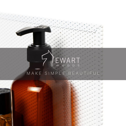 Close-up of a perforated metal wall shelf with an amber pump bottle and the EWART WOODS logo overlayed, featuring the slogan &