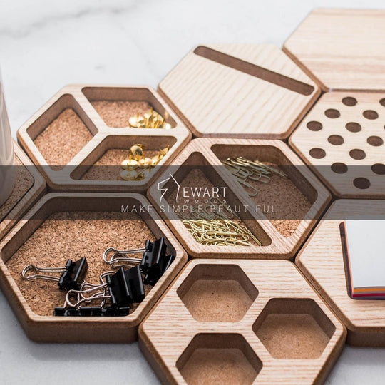 Hexagonal wooden desk organizers with cork inserts, arranged in a honeycomb pattern, holding office supplies. The &
