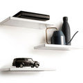 Set of three floating white shelves with a sleek, minimalist design and smooth, rounded edges. The top shelf holds a leather-bound book, the middle shelf supports a modern watering can and bottle, and the bottom shelf displays a classic car model.