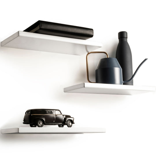Set of three floating white shelves with a sleek, minimalist design and smooth, rounded edges. The top shelf holds a leather-bound book, the middle shelf supports a modern watering can and bottle, and the bottom shelf displays a classic car model.