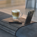 brown wooden sofa arm tray table on sofa arm with tv remote and coffee cup on it 