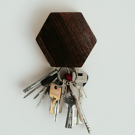 Close-up of a dark brown magnetic wooden key holder with several metal keys attached.