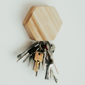 Hexagonal wooden key holder with natural wood grain, mounted on a white wall, holding a set of metal keys on a keyring.