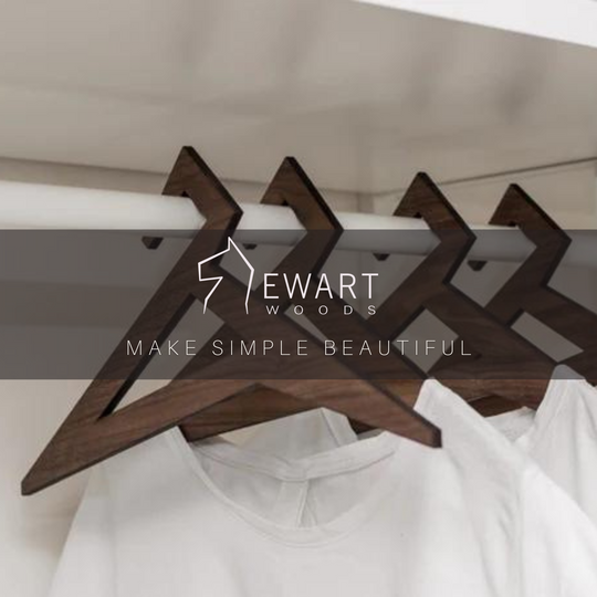 Wooden hangers in walnut finish with a geometric triangular design, holding white shirts in a closet. The image features the &
