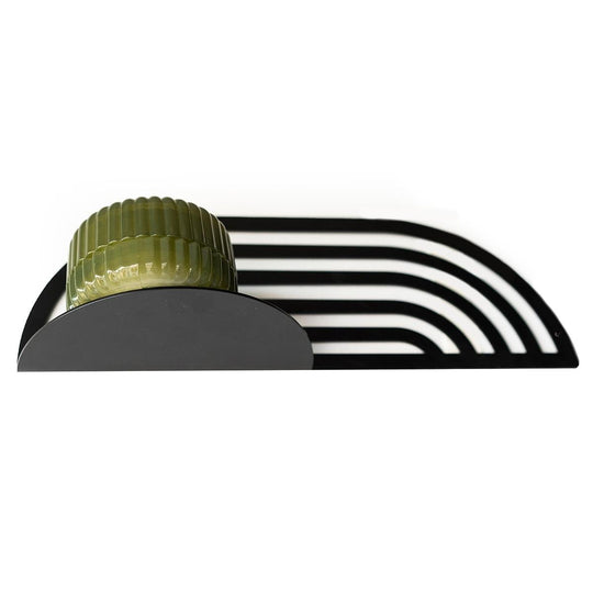 Decorative metal rack with an arched design, holding a small, rounded, ribbed container placed on its surface. The rack features parallel bars creating a sleek, modern look.