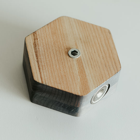 Close-up of the back of a hexagonal grey key holder, showing a metal screw and mounting hardware, with visible natural wood grain patterns.