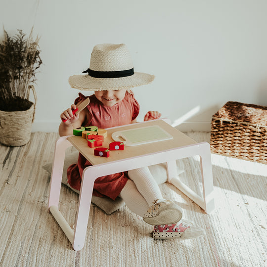 Child in a straw hat and red dress plays with wooden blocks at a farmer&