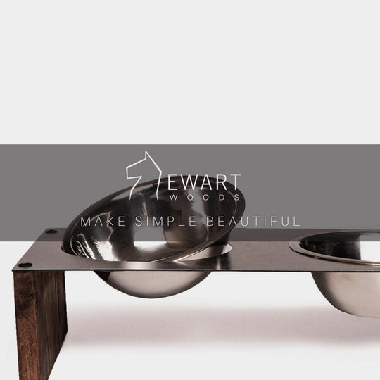 Close-up of a raised pet feeder with stainless steel bowls in a metal frame, supported by wooden sides. The &