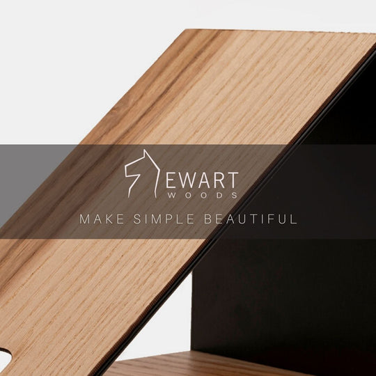 Close-up of a wooden and black metal phone stand, highlighting the smooth wood texture, with the Ewart Woods logo and the slogan &