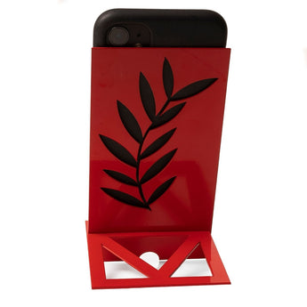 A smartphone positioned on a red, modern metal phone stand with a stylish leaf-shaped cutout in black. The stand features a geometric base, blending functionality with a decorative touch.