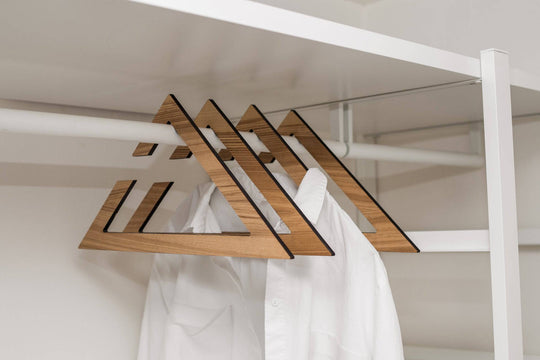 Stylish wooden hangers with a geometric triangular design, showcasing a rich paldau  finish. The hangers hold white t-shirts in a minimalist closet setup.
