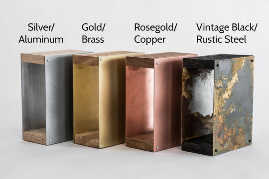 Four metal knife blocks in different finishes: silver/aluminum, gold/brass, rosegold/copper, and vintage black/rustic steel. Each block has a wooden top and base, displayed side by side against a plain background.