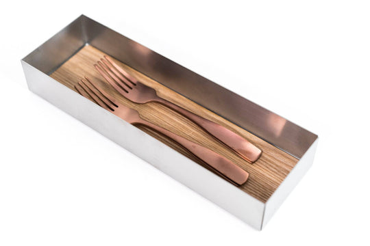 Long metal tray with a wooden bottom, containing two rose gold forks neatly aligned side by side.