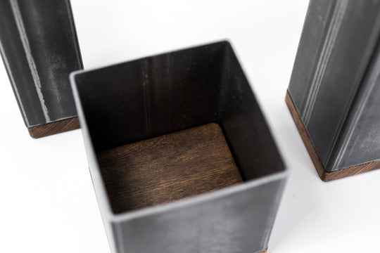 Close-up view of three black metal rectangular utensil holders with wooden bases, focusing on the open interior of the shortest holder, showing the wooden bottom surface