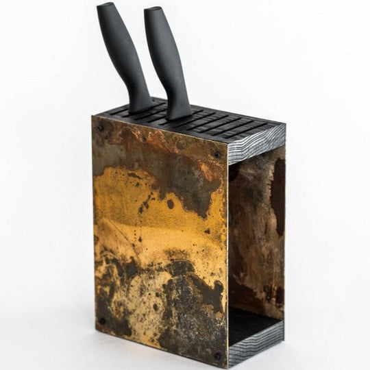 Rustic, industrial-style knife block with a weathered, patina-finished exterior and a wooden top, holding two black-handled knives. The block features a side slot for additional storage and is displayed against a white background.