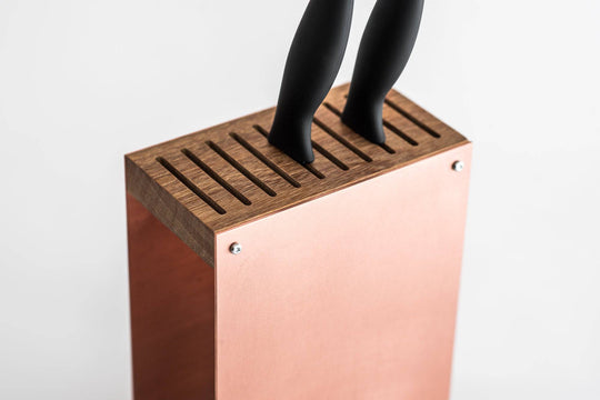 Rose gold knife block with a smooth metal finish, featuring a wooden top and base. The block has a modern, minimalist design and is displayed against a plain white background.