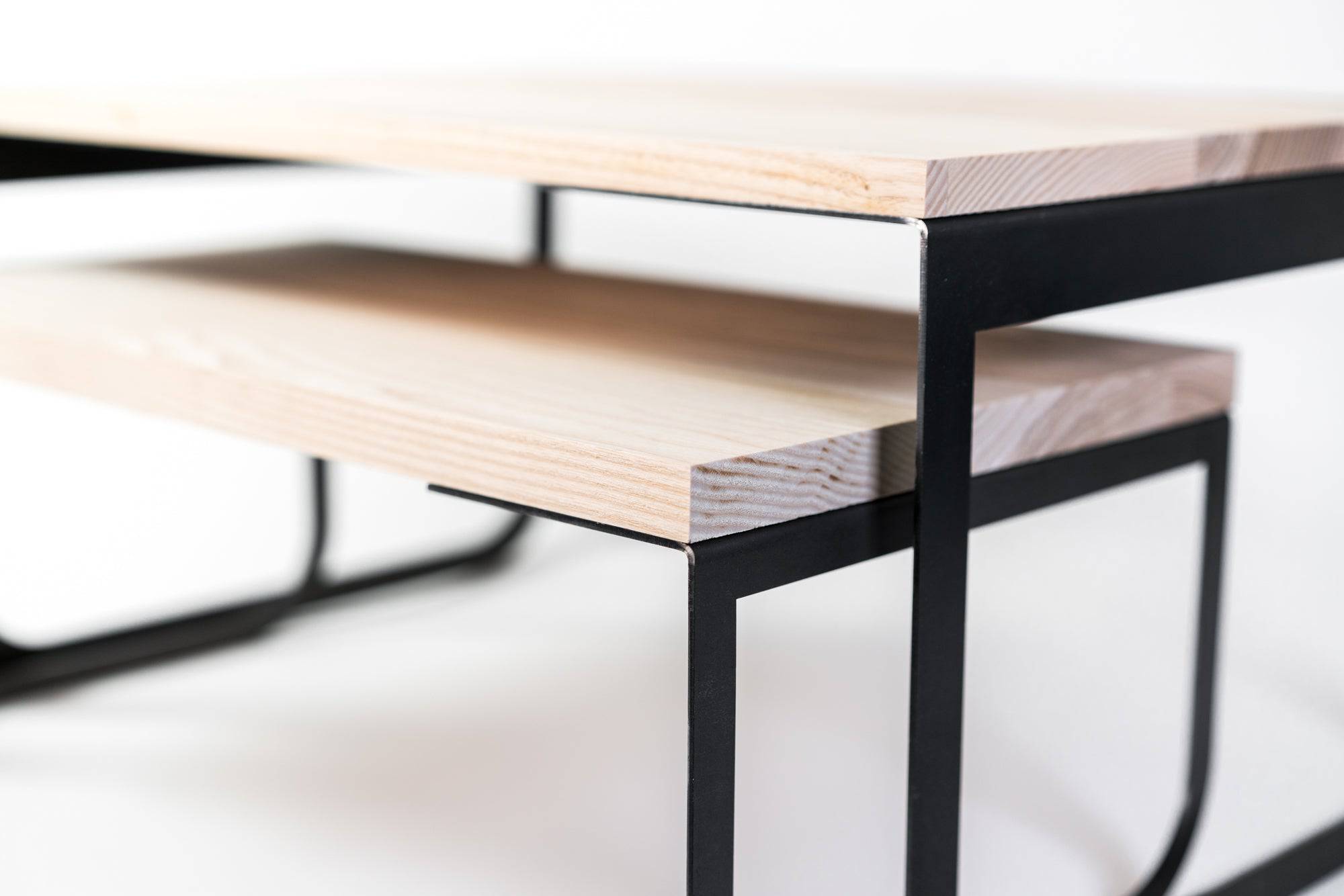 Close-up of a contemporary wooden coffee table with industrial black metal legs, showcasing a minimalist design with layered natural wood surfaces.