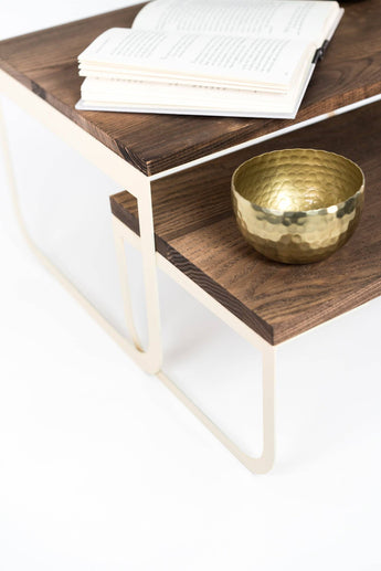 Contemporary tray set with rich wood tones and ivory metal legs, holding a textured gold bowl and a partially open book on the upper tier.