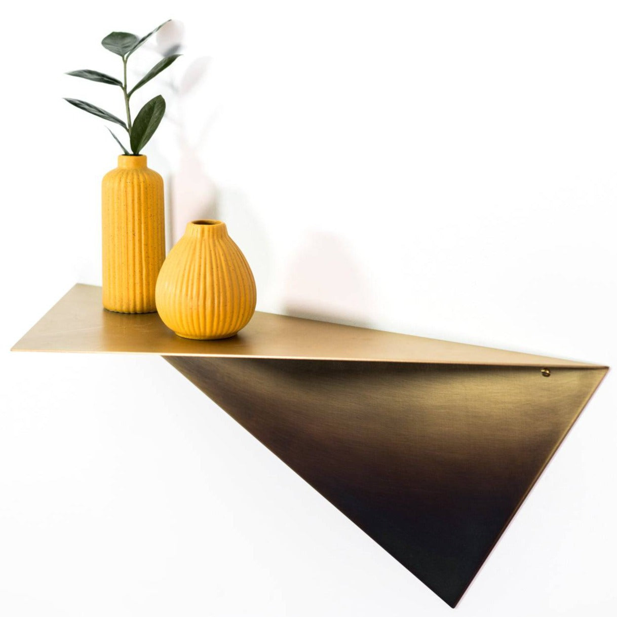 Modern triangular wall shelf in a brushed metal finish, adorned with two orange textured vases and a plant, creating a stylish and minimalist display.