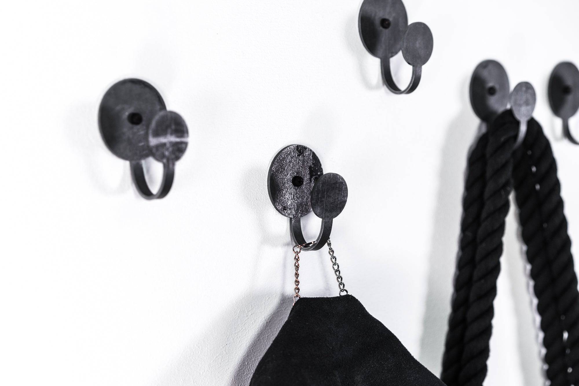 Set of three industrial-style black metal wall hooks with round bases, designed to hold ropes, bags, and accessories, showcasing a sleek and modern look.