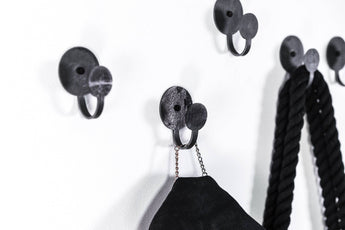 Set of three industrial-style black metal wall hooks with round bases, designed to hold ropes, bags, and accessories, showcasing a sleek and modern look.