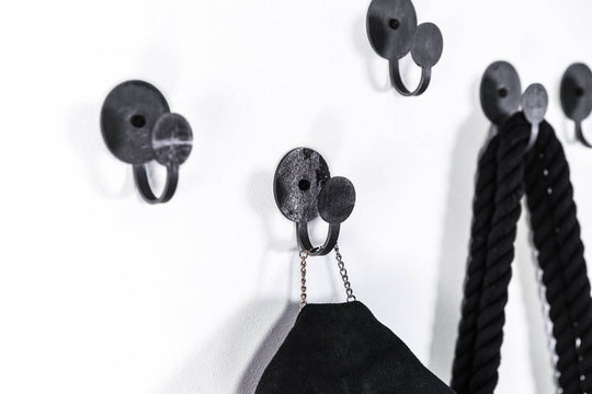Set of three industrial-style black metal wall hooks with round bases, designed to hold ropes, bags, and accessories, showcasing a sleek and modern look.