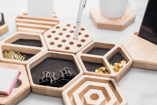 Hexagonal wooden desk organizers with compartments lined with fabric, holding paper clips, thumbtacks, and binder clips. The setup includes a pen holder, a cardholder, and matching coasters, blending functionality with stylish organization.