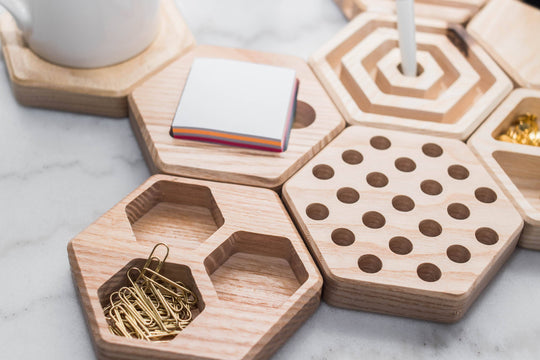 Close-up of hexagonal wooden desk organizers, showcasing compartments holding paper clips, sticky notes, and thumbtacks, along with a pen holder and geometric design details.