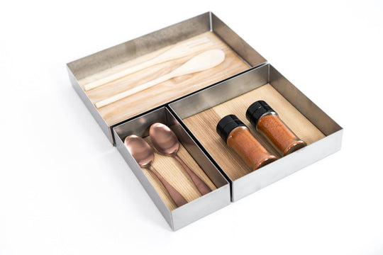 Kitchen drawer organizer with wooden utensils, copper spoons, and spice jars in metal and wood compartments designed for utensil storage.