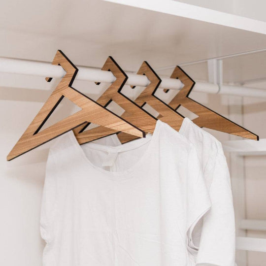 Set of wooden hangers in ash wood finish, featuring a sharp geometric design, holding white t-shirts in an organized closet.