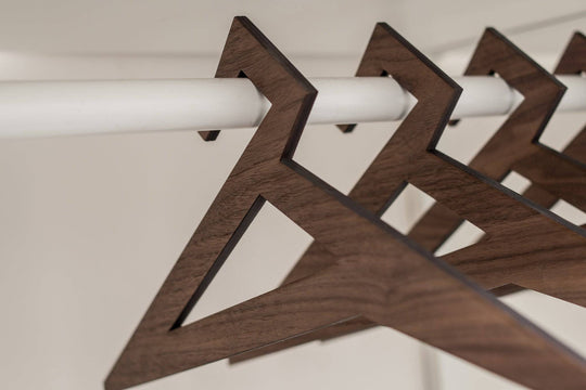 Geometric wooden hangers with a triangular design and rich walnut finish, holding a white shirt in a minimalist closet.