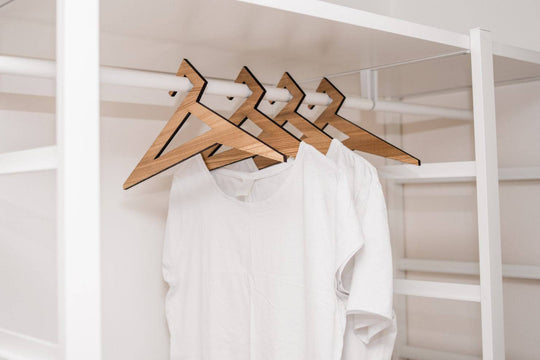 Set of wooden hangers in ash wood finish, featuring a sharp geometric design, holding white t-shirts in an organized closet.