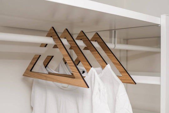 Wooden hangers in paldau finish with a geometric triangular design, holding white shirts in a neatly organized closet.