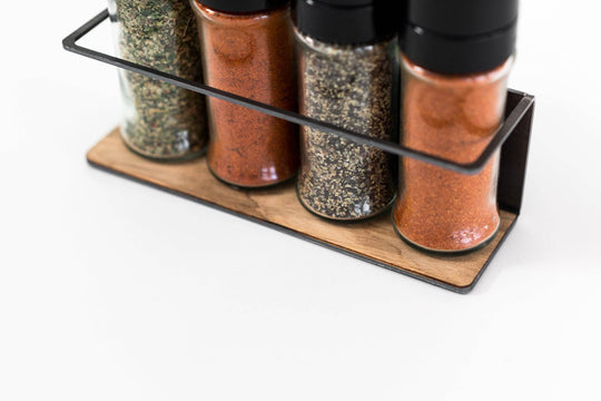 Spice rack with a black metal frame and a textured wooden base, holding four spice jars in a sleek, compact design, perfect for organizing spices in your kitchen.