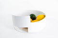 Contemporary white metal bowl with a layered, modern design, holding vibrant lemons and limes on a white background.