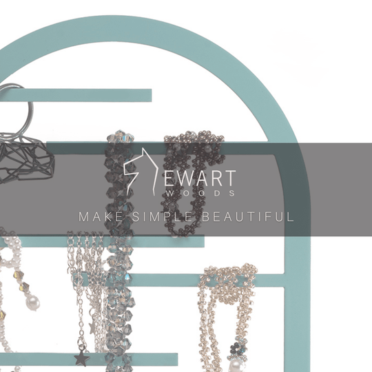 Teal arch-shaped jewelry holder with hanging necklaces and bracelets, featuring Ewart Woods branding and tagline &