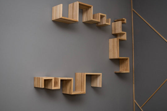 Three zigzag-shaped floating shelves made of light-colored wood with a visible grain pattern, featuring clean, sharp edges and varying heights. The shelves are arranged in a staggered pattern on a gray wall.