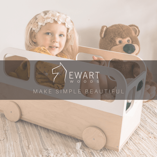 Child playing inside a minimalist wooden bus-shaped storage box, designed with natural wood and white accents. Ewart Woods branding is visible with the slogan &