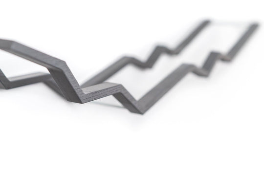 Close-up of a wall-mounted gray zigzag toilet paper holder with a textured wood surface, showcasing the intricate zigzag design with metal bars.